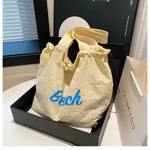 Detail of beige wrinkled fabric tote bag with blue Beach lettering and drawstring closure