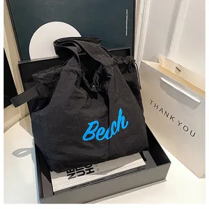 Close-up of black canvas tote bag with blue Beach text in a stylish gift box setup