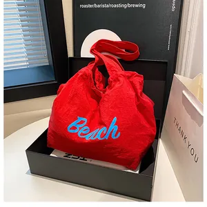 Detail of red Beach tote bag with blue embroidery, black gift box, and white paper bag