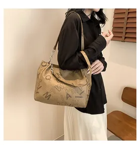 Macro shot of large khaki leather tote bag with black letter patterns and metal chains