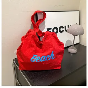 Detail of red oversized tote bag featuring a bright blue Beach script and textured fabric