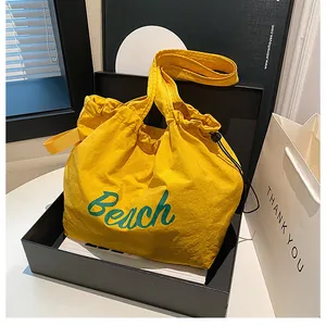 Detail view of yellow drawstring beach tote bag with green text inside black display box