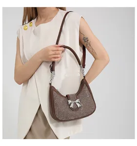 Detail view of brown crescent handbag featuring silver rhinestones and metal bow buckle