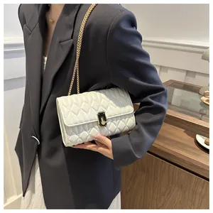 Close-up of white quilted chain bag with gold hardware worn on a dark grey suit jacket