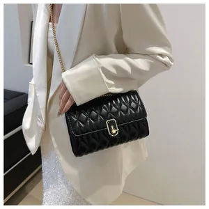 Detail of black quilted leather crossbody bag with gold chain strap on white blazer