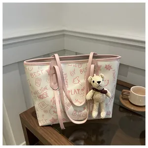 Detail of large tote bag with pink trim, bear charm, and graffiti prints on a wood table