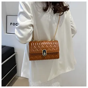 Detail of brown quilted chain bag with gold metal clasp on a white suit model