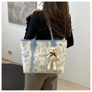 Large beige tote bag with blue graffiti prints and a cute teddy bear charm on model