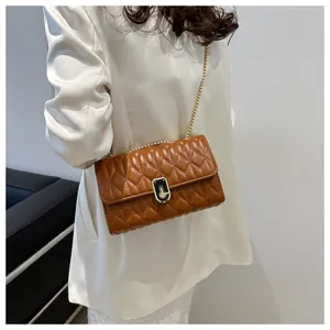 Brown quilted crossbody bag with gold chain strap worn over a white oversized blazer