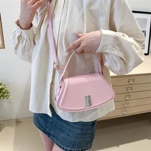 Pink crossbody handbag with curved design and silver metal buckle in stylish home setting