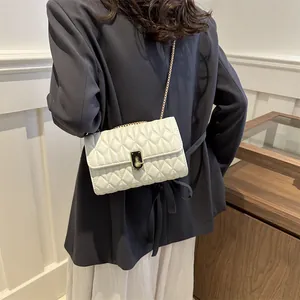 Elegant cream quilted crossbody bag with gold chain strap on a blazer-clad model