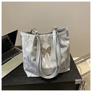 Detail of silver tote bag with crinkled texture and liquid metal butterfly ornament