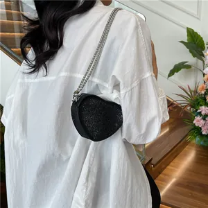 Chic black sequin heart-shaped mini crossbody bag with silver chain strap worn by model
