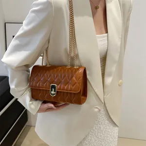 Brown quilted crossbody bag with gold chain strap shown on model in white blazer