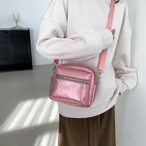 Pink metallic crossbody camera bag with adjustable strap worn by model in minimalist setting