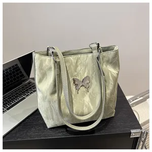 Close-up of a light green pleated tote bag featuring a metallic silver butterfly detail