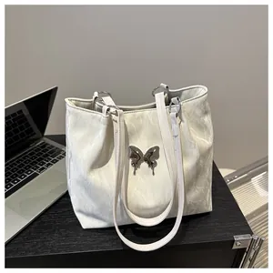 Detail of soft faux leather tote bag with liquid metal butterfly charm on office desk
