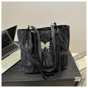 Detail of black tote bag with pleated texture and silver butterfly buckle in office setting