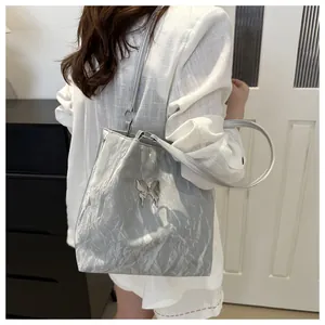 Detail of silver metallic tote bag featuring a decorative butterfly buckle and soft texture