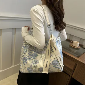Large floral tote bag with blue print and chain strap worn by a model in interior
