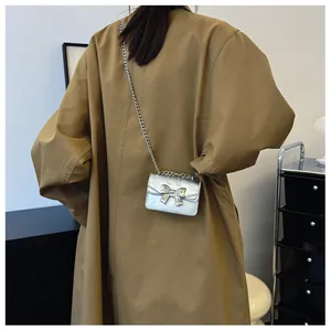 Silver bow chain mini bag shown crossbody on a brown trench coat for styling detail