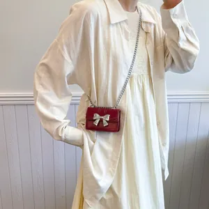 Mini red crossbody bag with silver bow accent and chain strap worn by a model