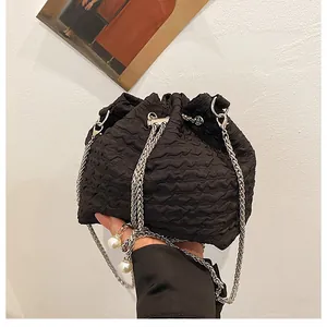 Détail du sac seau noir à cordon avec texture matelassée et détails de chaîne perlée