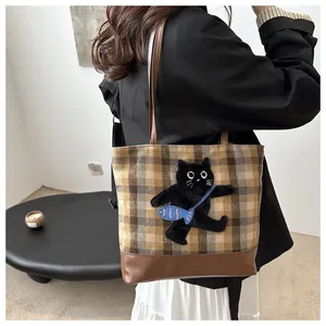 Détail du sac cabas à carreaux avec écusson chat en 3D et bandoulières en cuir brun