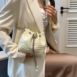 Sac seau plissé beige chic avec cordon perlé et chaîne en métal porté par un mannequin