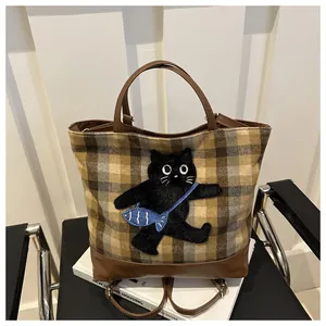 Détail du sac cabas à carreaux avec applique chat et base en cuir sur un livre blanc