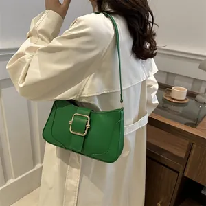 Green shoulder bag with gold buckle worn by model in a stylish trench coat