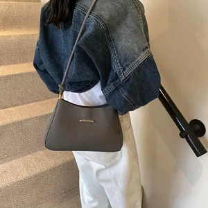 Brown textured underarm bag with gold hardware worn by model in casual outfit
