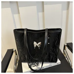 Dettaglio della borsa tote nera con trama stropicciata ed emblema farfalla argento