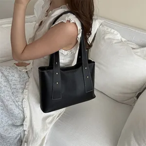 Minimalist black leather tote bag with white contrast stitching and gold rivets detail