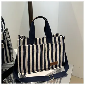 Detail of canvas tote bag with blue stripes featuring front pockets and brown leather label