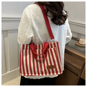 Detail of red and white striped canvas tote bag with adjustable strap and fashion label