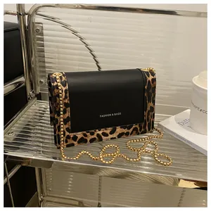 Detail of leopard print small square bag with gold chain strap on minimalist glass shelf
