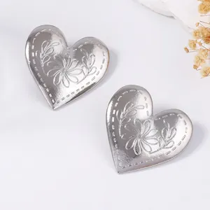 Detalle de pendientes de corazón plateados con motivos florales en relieve y borde texturizado
