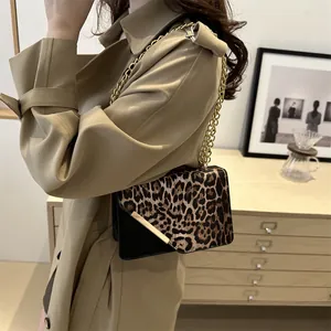 Leopard print and black leather shoulder bag with gold chain strap in home setting