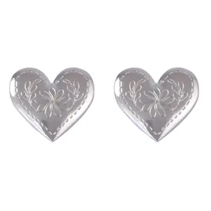 Primer plano de pendientes de corazón plateados con grabado floral y de hojas