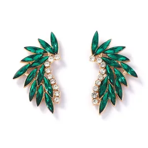 Detailed macro shot of gold feather earrings featuring emerald green marquise cut stones
