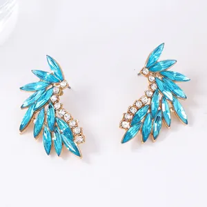 Macro detail of gold-plated wing earrings with marquise blue and white zircon stones