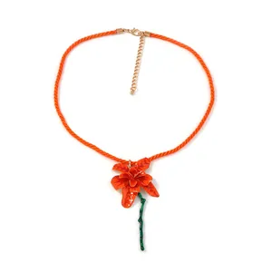 Makro-Detail des roten Blumenanhängers an einer orangefarbenen geflochtenen Kordelkette