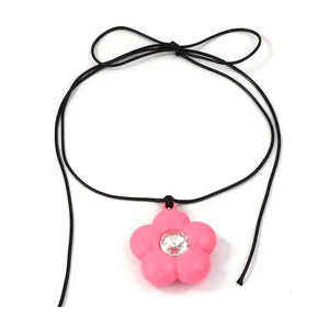 Gros plan du pendentif fleur en résine rose avec strass sur cordon noir à nœud