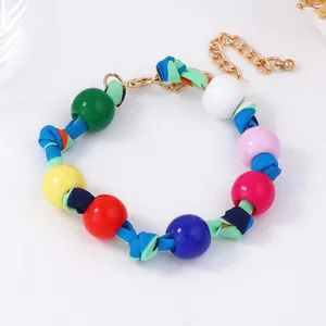 Macro detail of colorful beaded bracelet with braided fabric rope and golden metal clasp