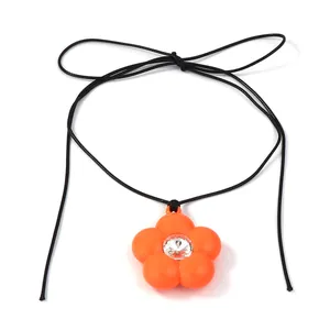 Vue détaillée du pendentif fleur 3D orange avec strass blanc sur un cordon noir tressé