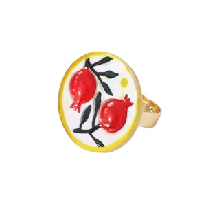 Nahaufnahme eines goldenen Retro-Rings mit handgemaltem Granatapfel und grünen Blättern