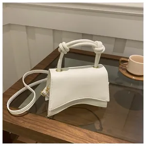 Detail of white textured mini bag with knotted handle and curved base on wooden table