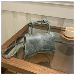 Detail of vintage denim crossbody bag with knot handles and curved base on a wooden table