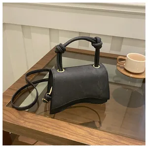 Detailed shot of a black hourglass handbag with knotted handle on a wooden cafe table